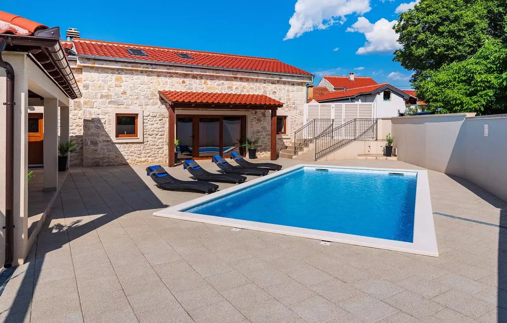 An outdoor swimming pool sits beside a stone house and sun loungers.