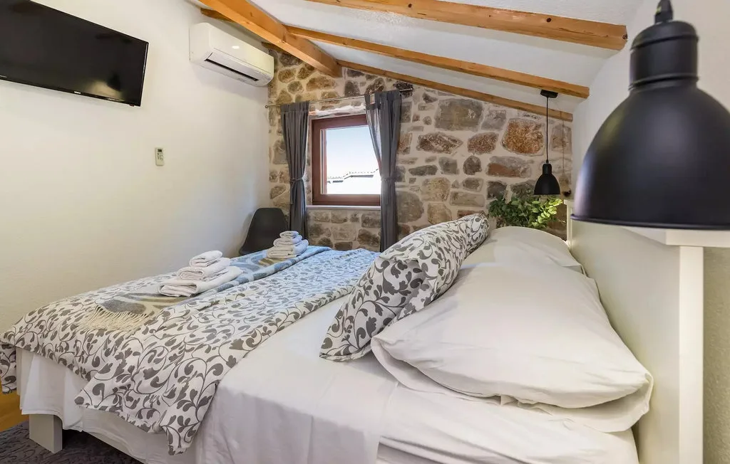 A bedroom with two beds, patterned bedding, and an exposed stone wall.