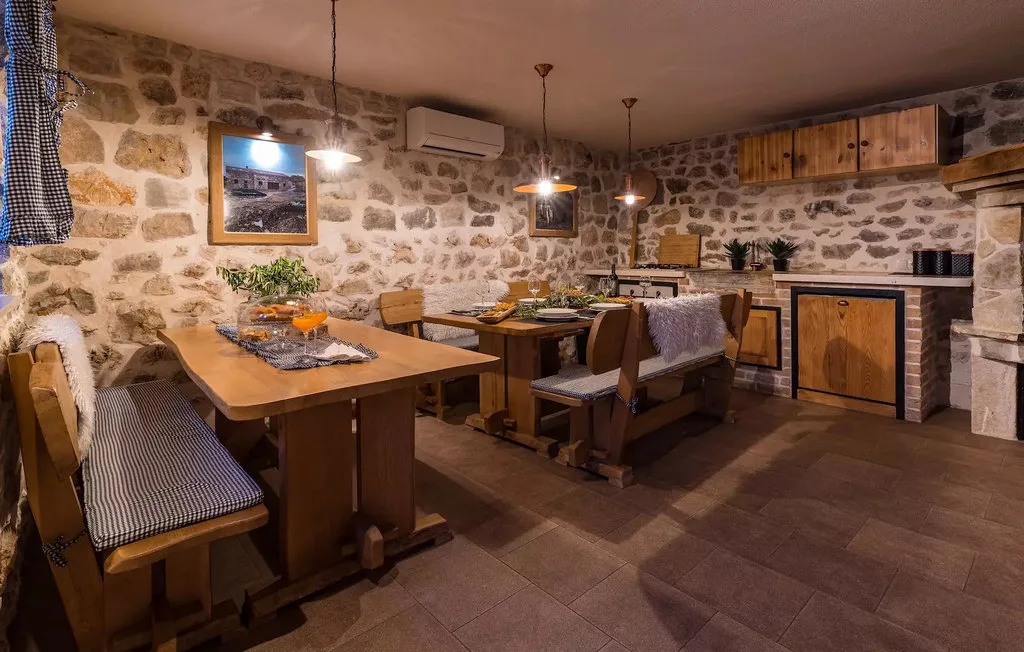 A rustic dining area with wooden tables beside a stone-walled kitchen.