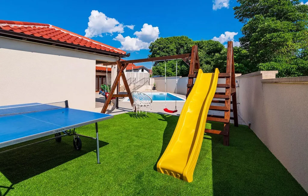 An outdoor play area with a yellow slide, swings, and a table tennis table.