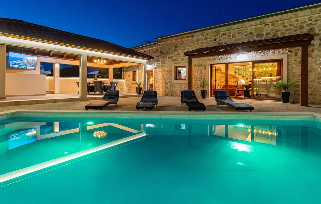 A swimming pool beside a stone building, with lounge seating along the edge.