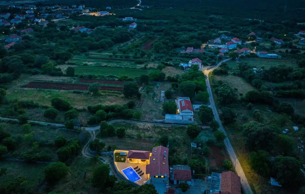 An aerial view of a rural settlement with scattered homes, fields, and a winding road.