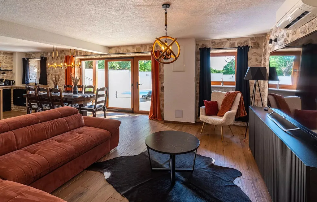 A living and dining area with a sofa, dining table, and windows opening onto a patio.