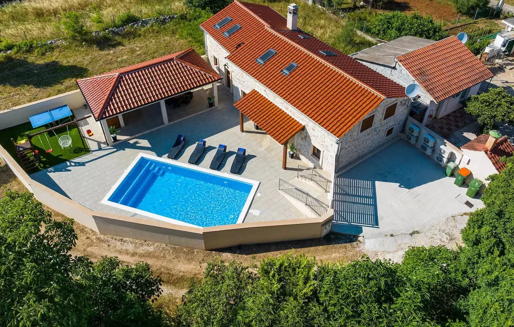 Aerial view of a house and swimming pool surrounded by paved patio space.