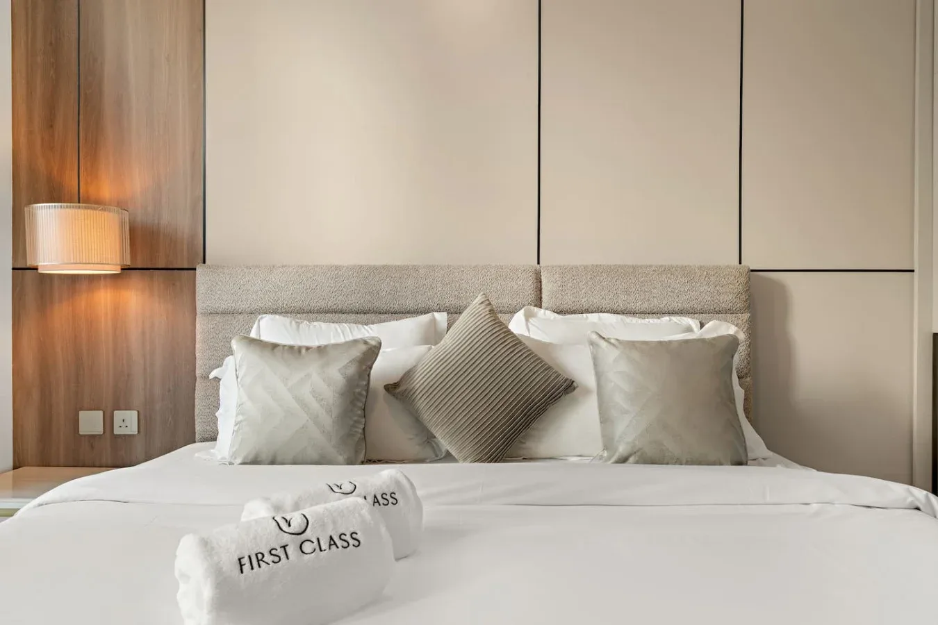 Una cama bien tendida con varias almohadas está junto a un cabecero acolchado.
