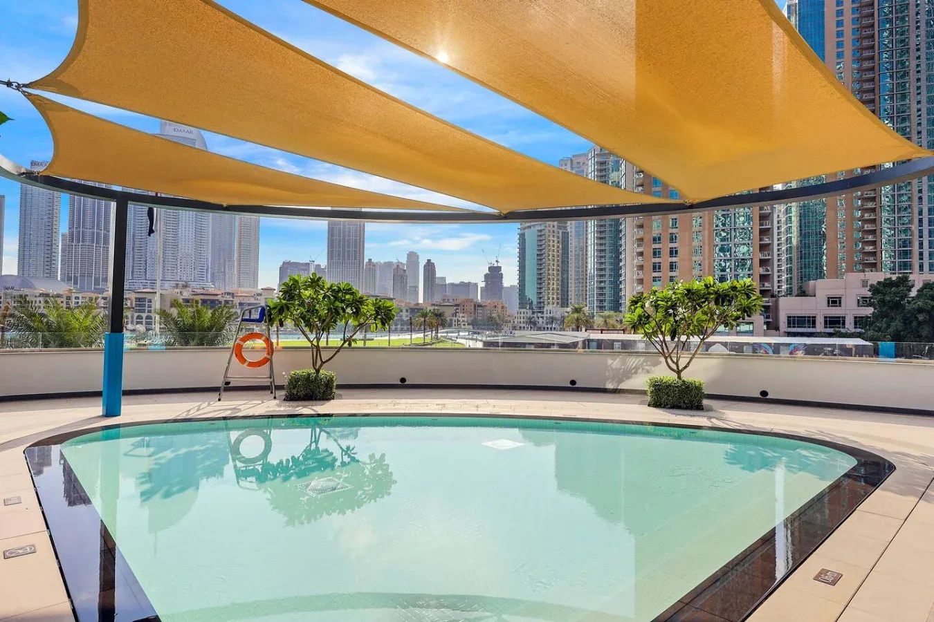 Una piscina en la azotea está bajo toldos de sombra, con edificios altos al fondo.