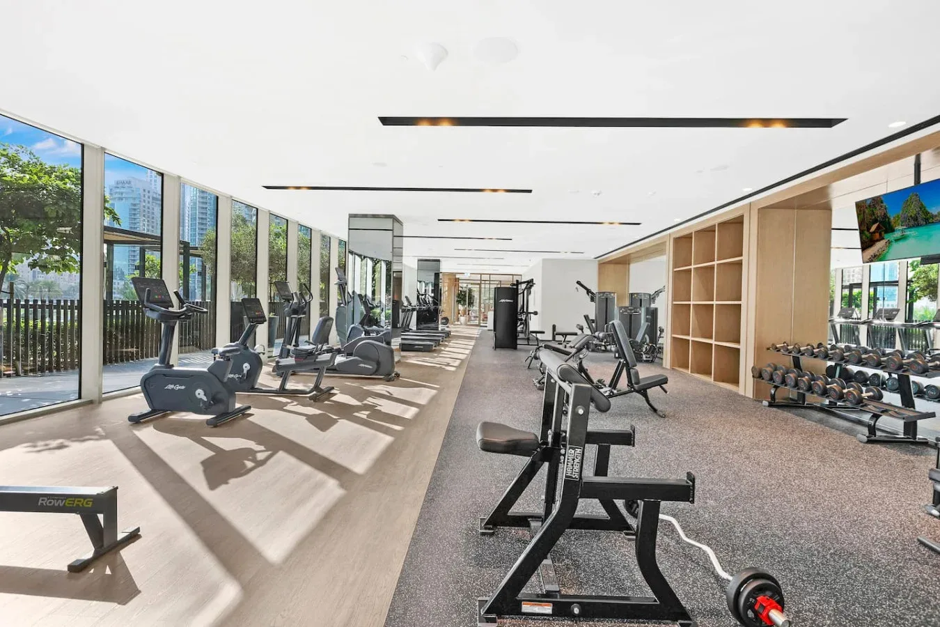 Un gimnasio luminoso con máquinas de ejercicio junto a ventanales.