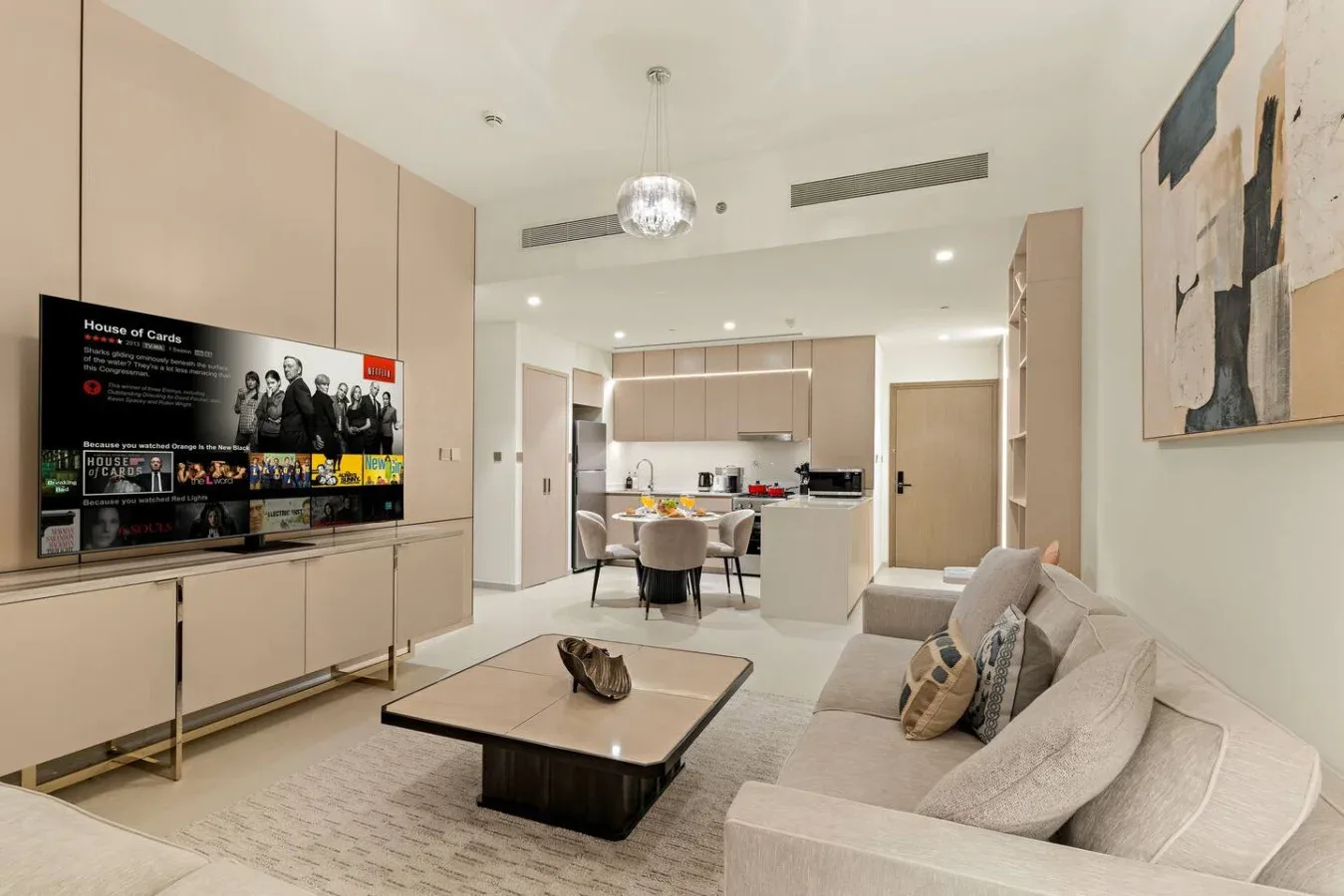 Una sala de estar moderna se abre a un comedor y una cocina, con un televisor en la pared.