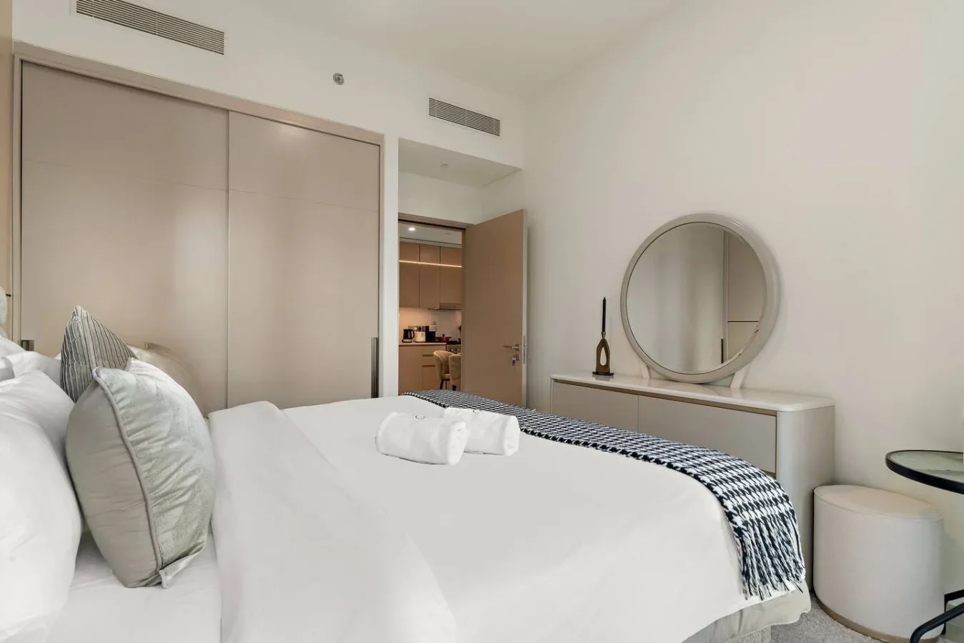 Un dormitorio con una cama tendida y un espejo redondo sobre una consola.