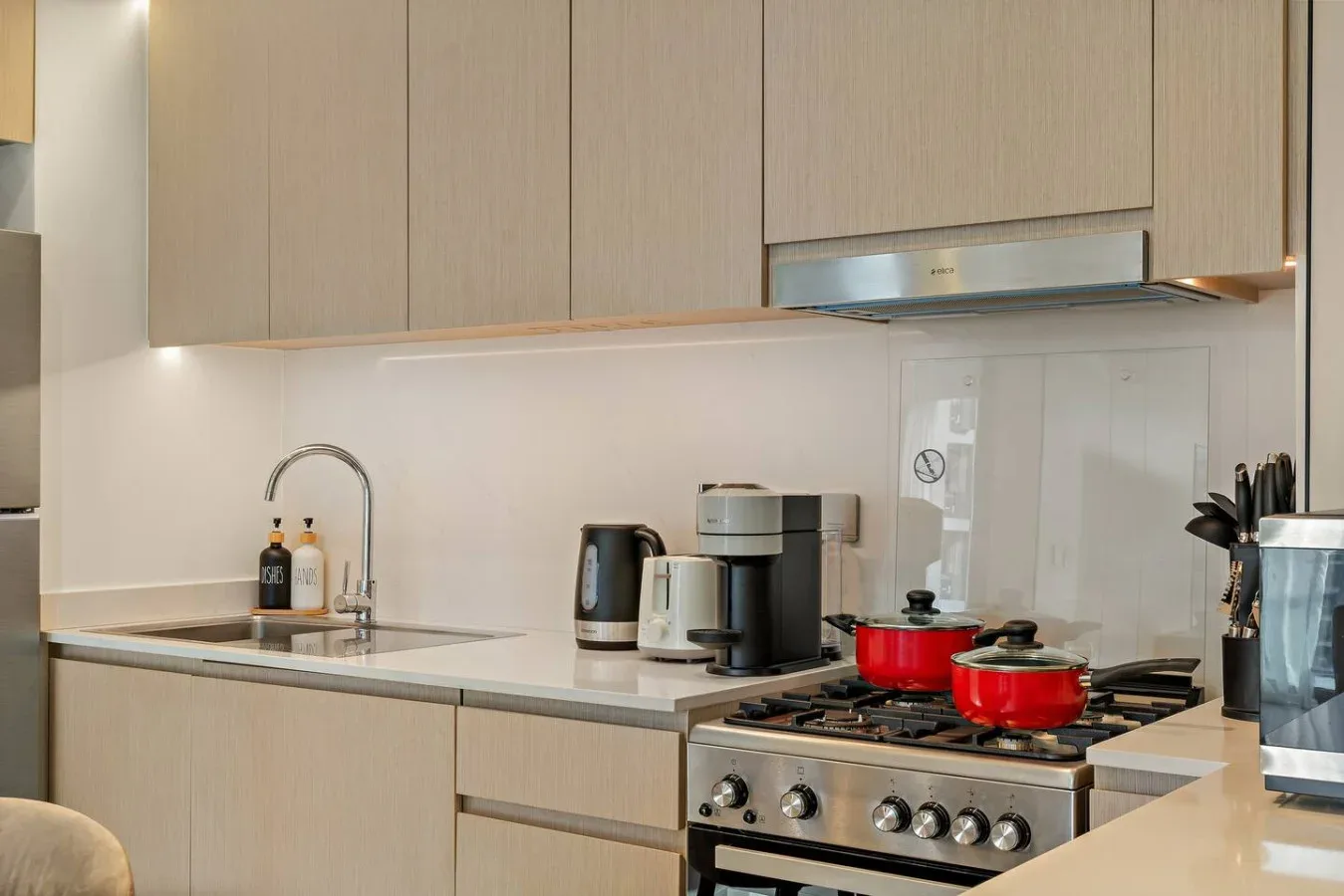 Una cocina moderna con electrodomésticos sobre la encimera y ollas en la estufa.