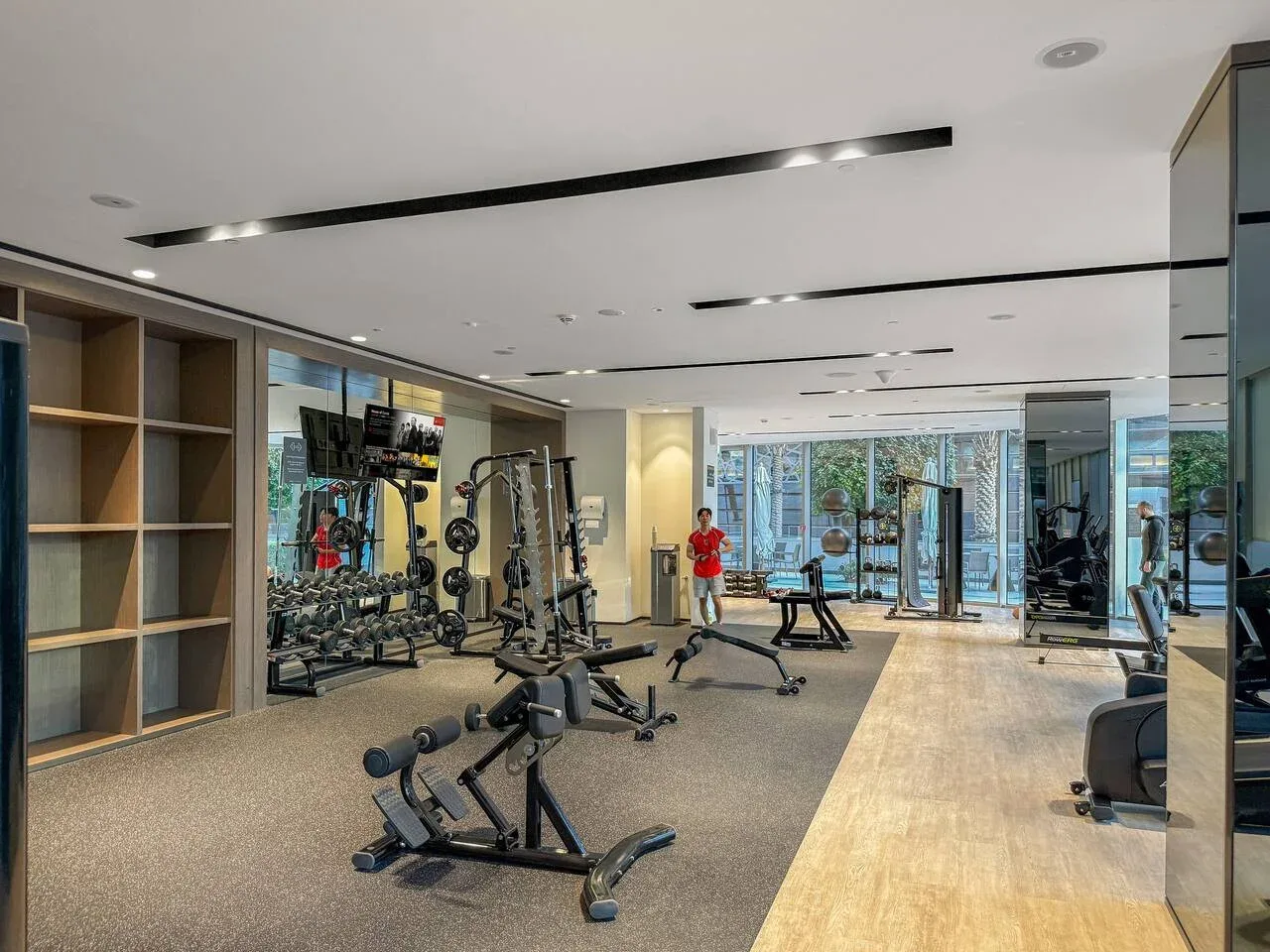 Un gimnasio con máquinas de ejercicio, pesas y un pasillo con suelo de madera.
