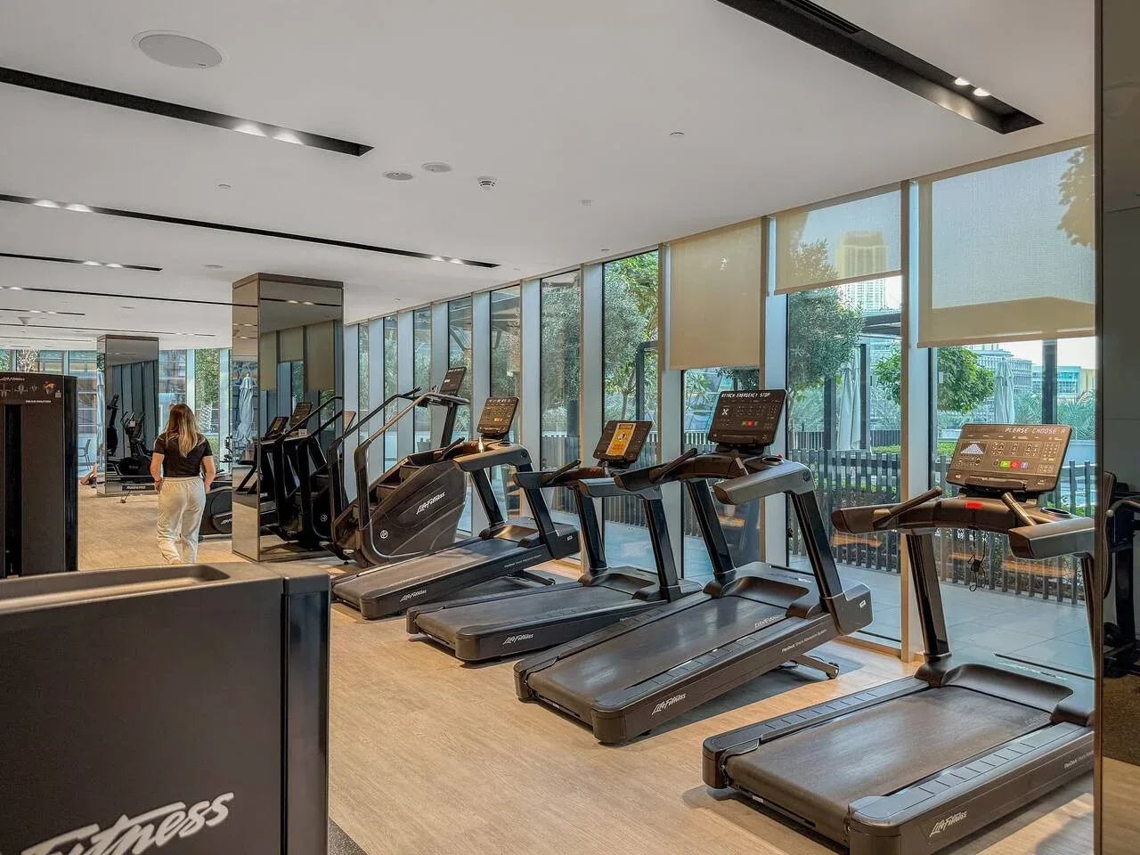 Un gimnasio con cintas de correr y otros equipos de ejercicio junto a grandes ventanales.