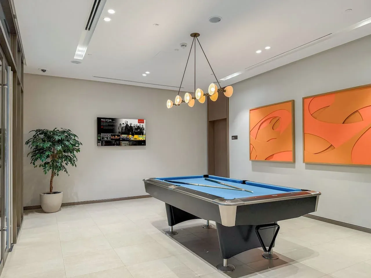 Una luminosa sala de juegos tiene una mesa de billar, cuadros y una planta en maceta.