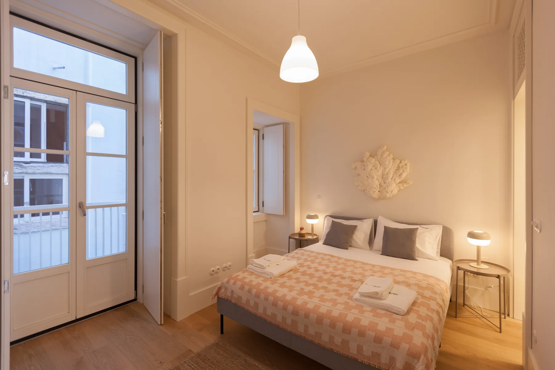 Un dormitorio con una cama, mesitas de noche y puertas acristaladas altas.