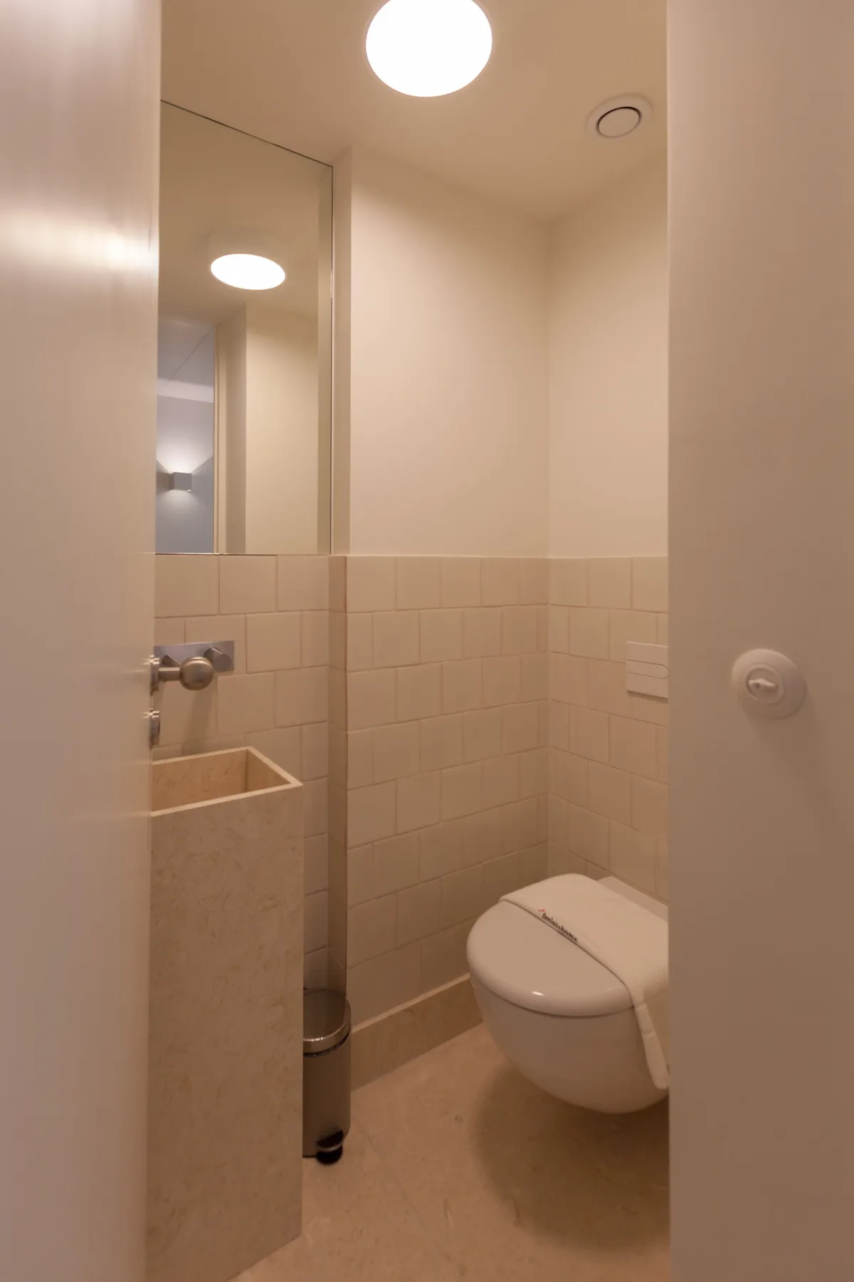 Un baño con un inodoro suspendido y un lavabo con azulejos.