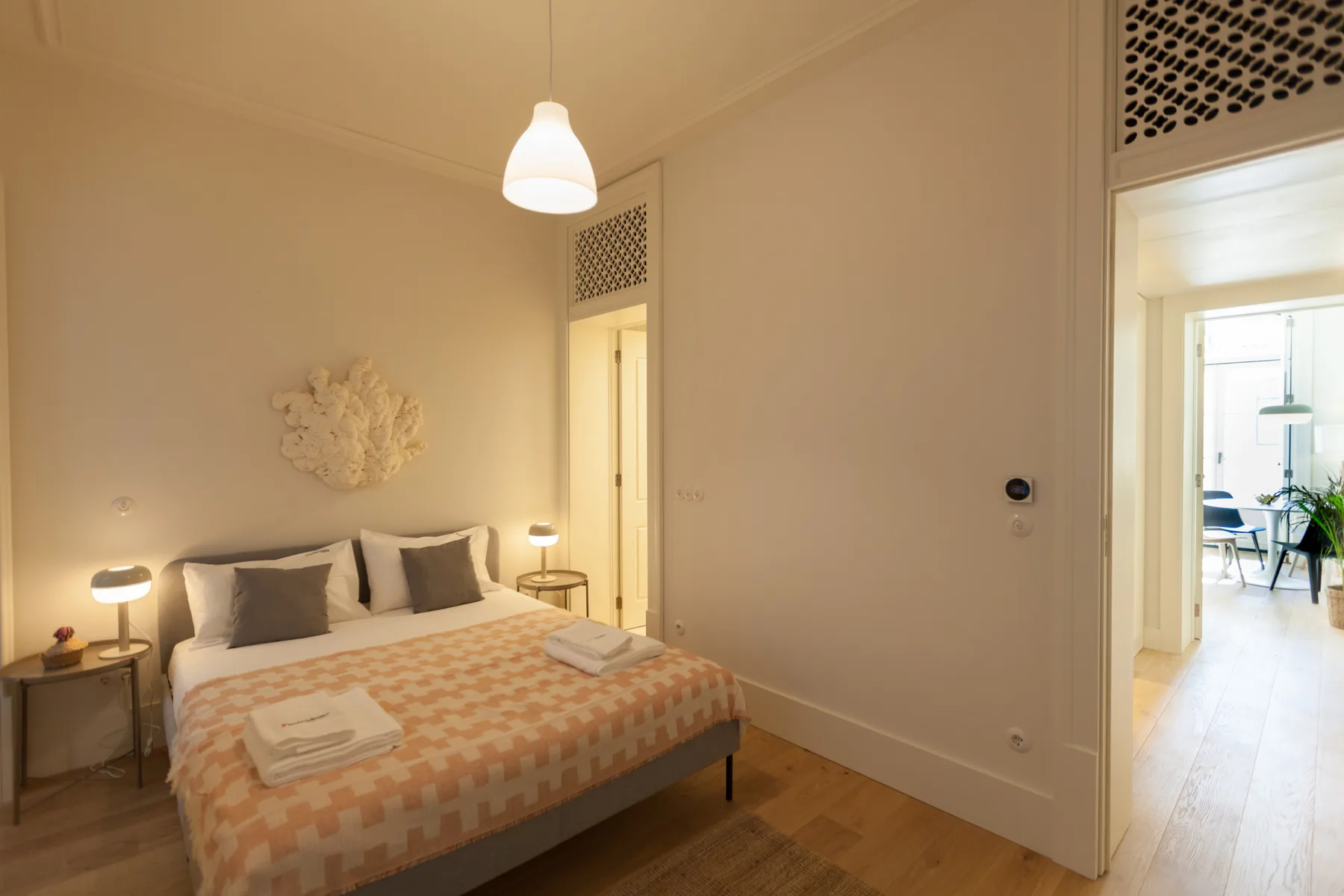 Dormitorio con una cama, mesillas de noche y una puerta a una habitación más luminosa.
