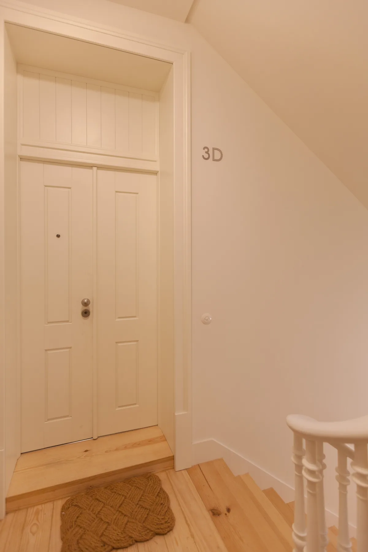 Una puerta blanca da a un rellano de madera con un felpudo tejido.
