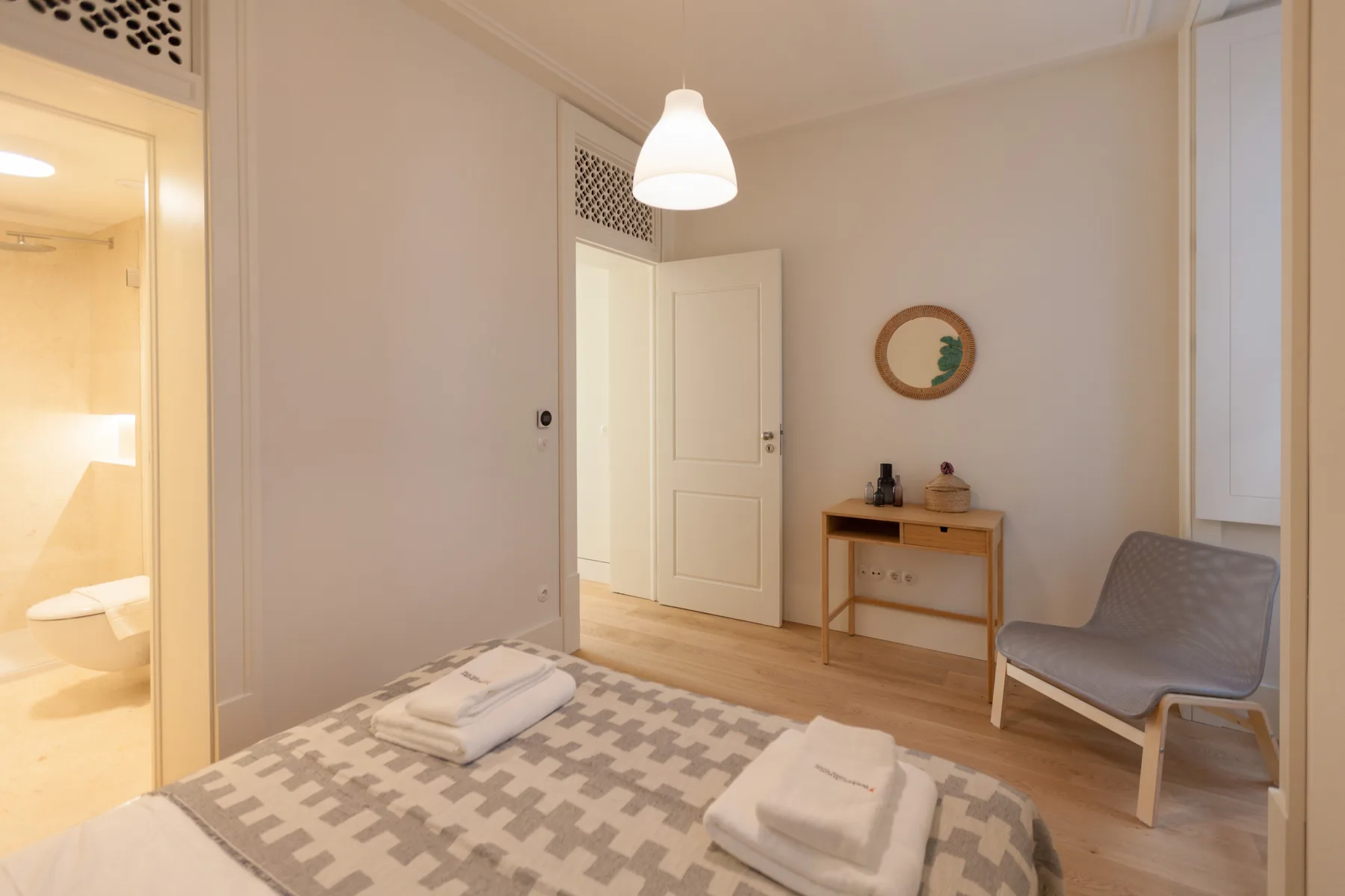 Un dormitorio con la cama hecha, una mesa pequeña y asientos junto a una puerta abierta.