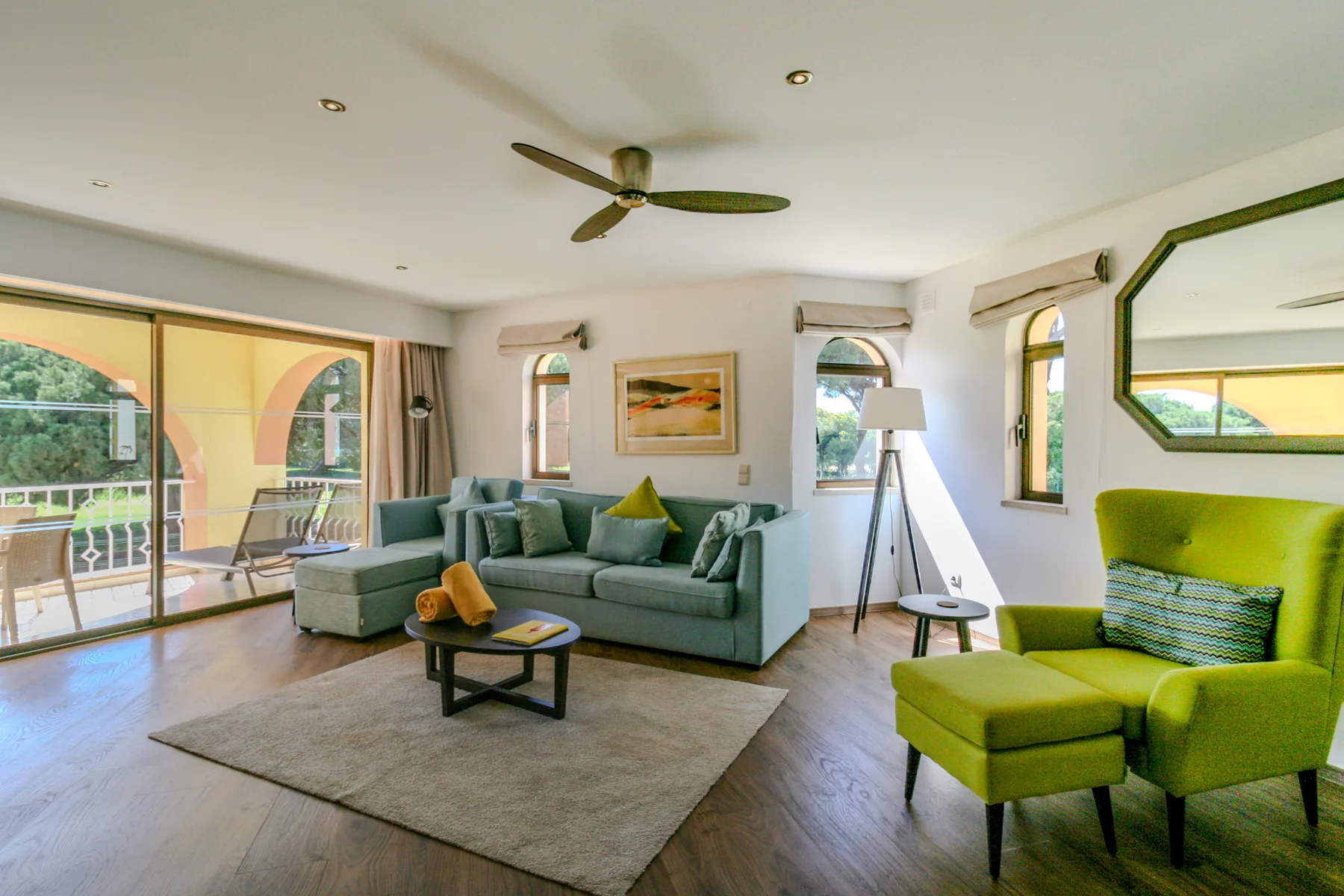 A bright living room with seating, a rug, and large windows opening onto a balcony.
