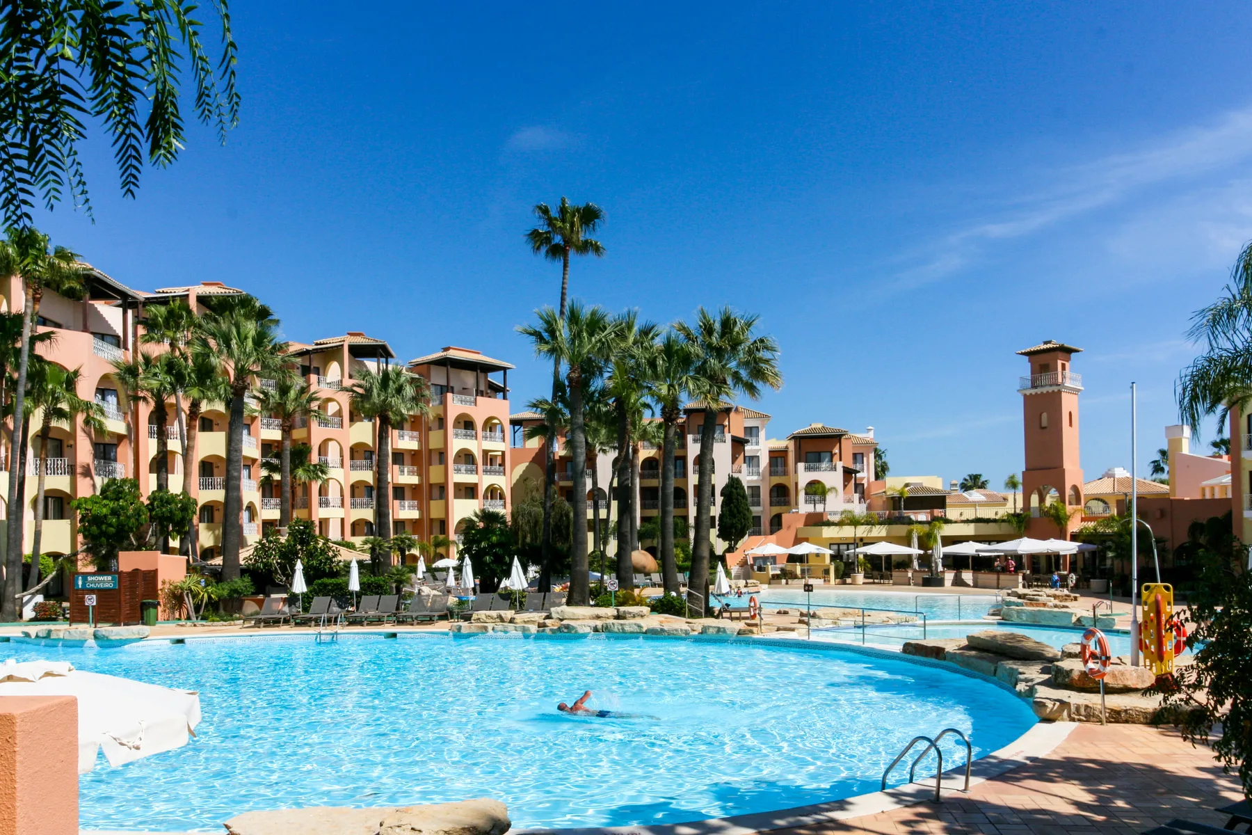 A swimming pool in front of an apartment complex, surrounded by palm trees.