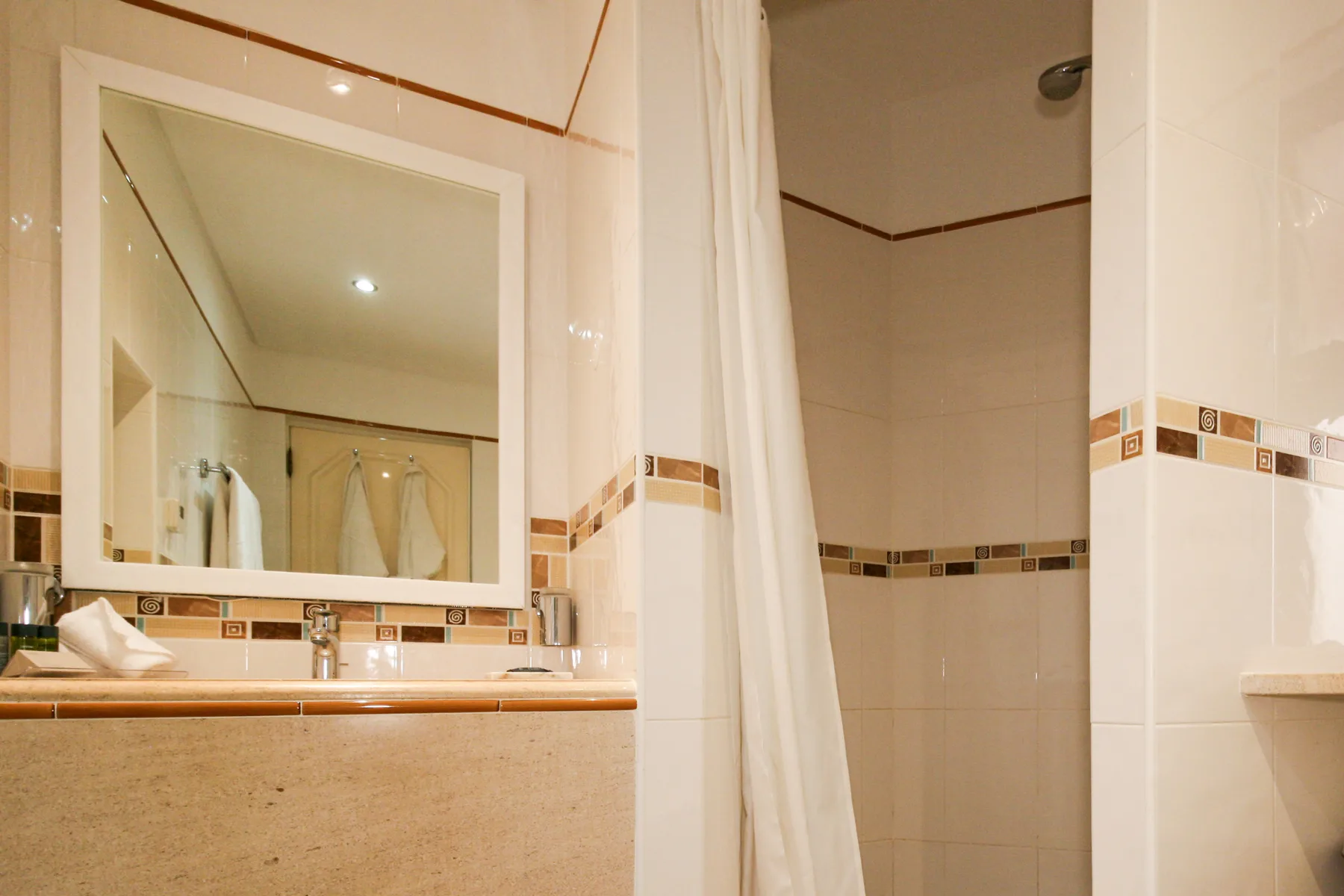 A bathroom with a wide mirror above the sink and a shower behind a curtain.