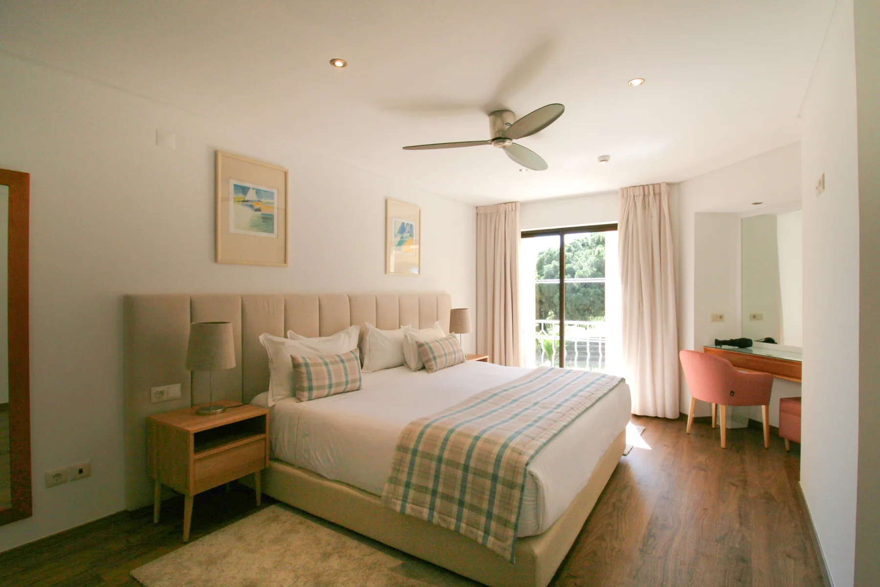 A bright bedroom with a double bed, bedside tables, and a glass door to the balcony.