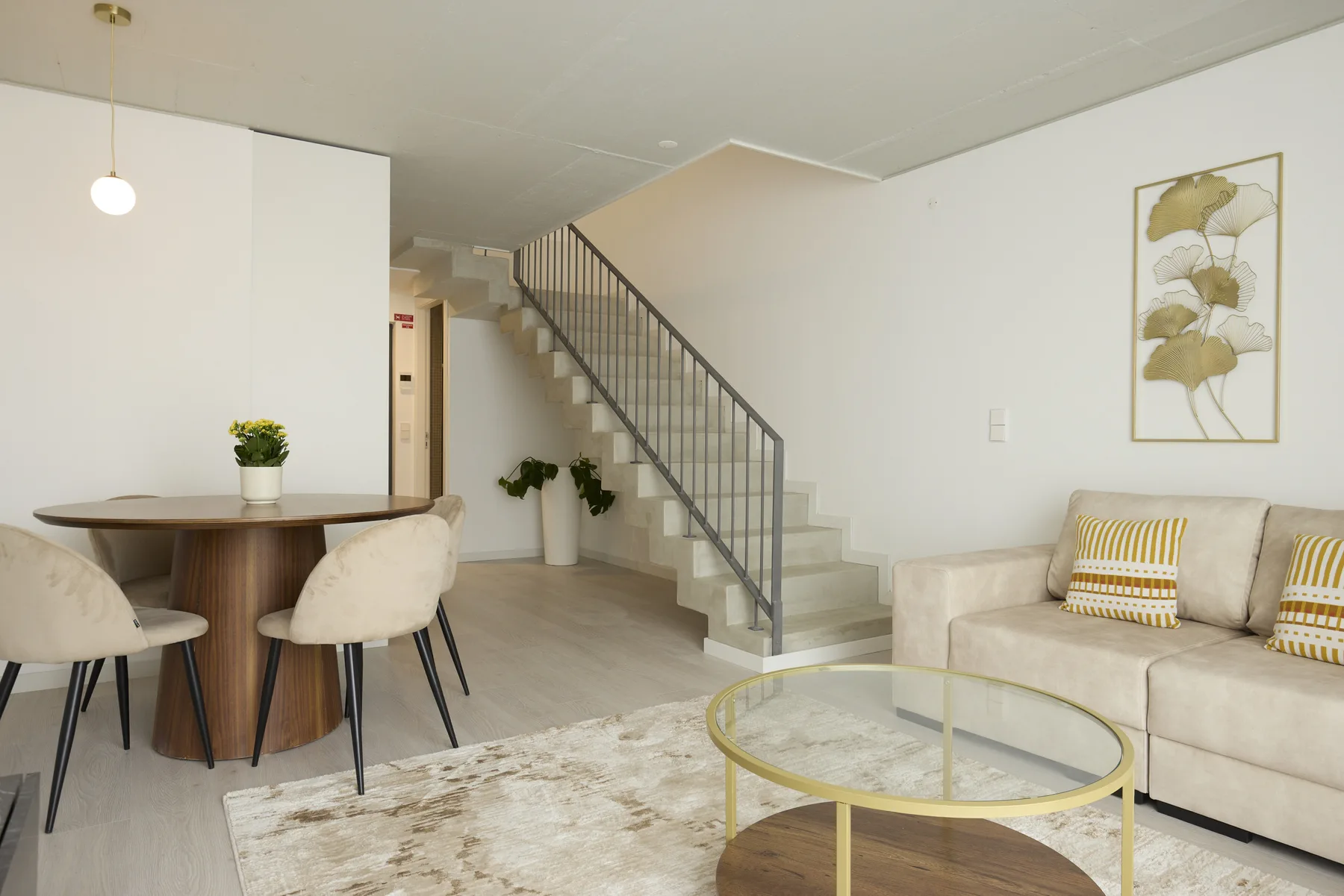 Una luminosa sala de estar y comedor con una escalera y asientos en tonos neutros.