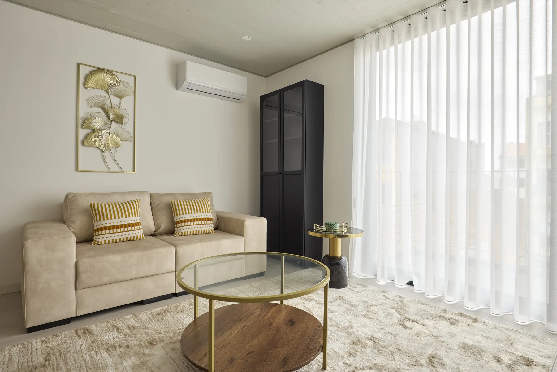 Una sala luminosa con asientos beige, una mesa de centro de cristal y cortinas translúcidas.