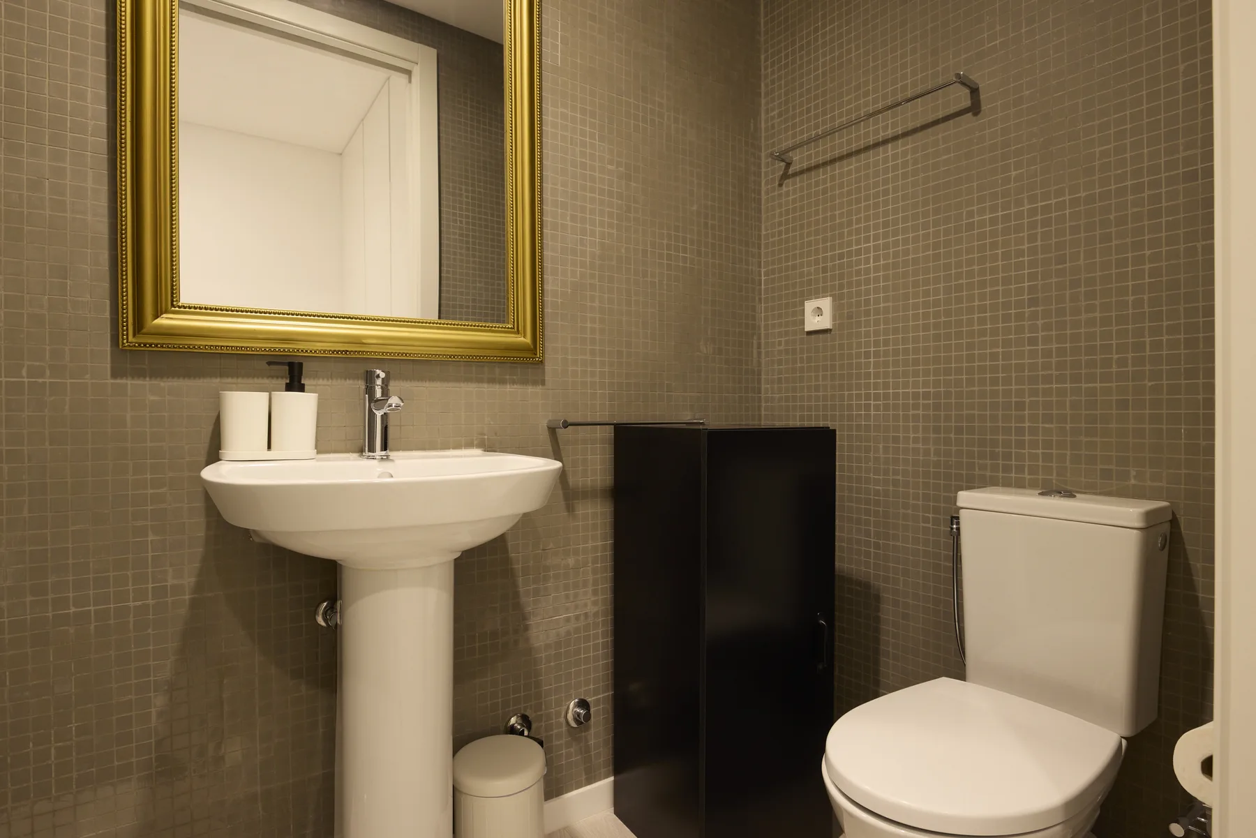 A bathroom with a pedestal sink, toilet, and dark tiled walls.