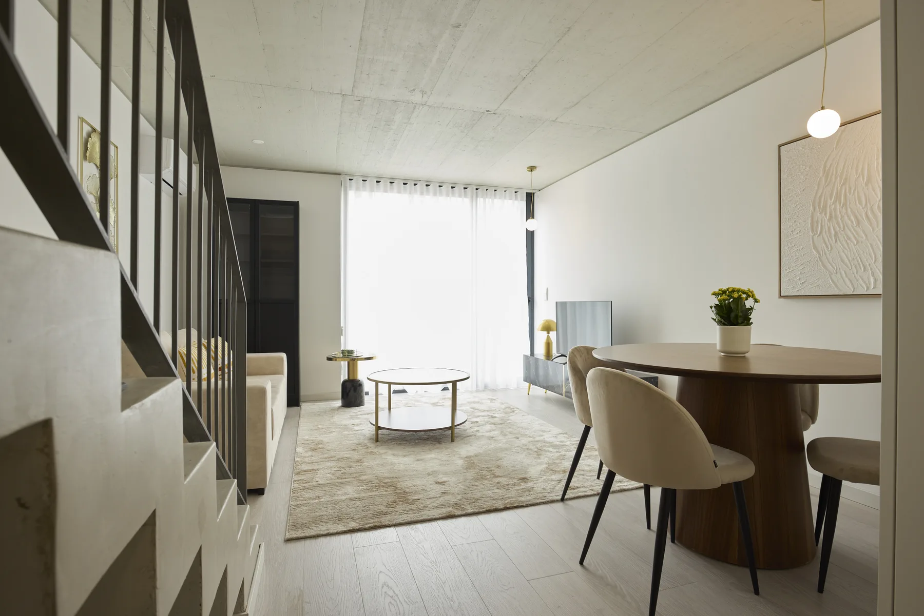 Una luminosa sala de estar y comedor con alfombra, mesa y escalera.