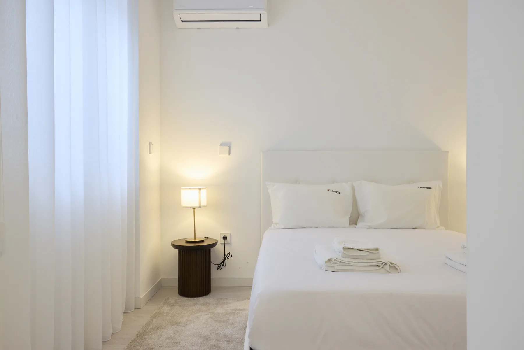 A bright bedroom with a neatly made bed and a bedside lamp.