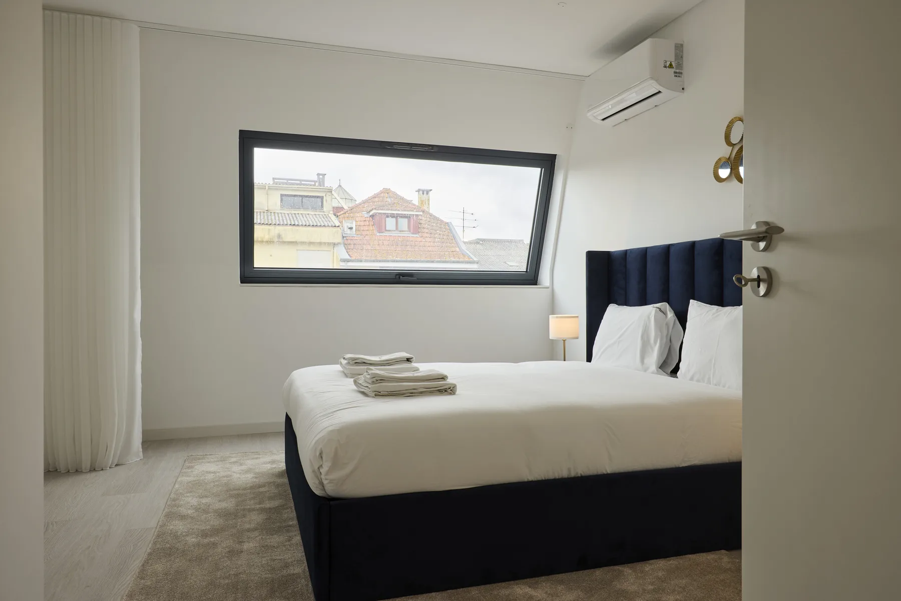 Un dormitorio con una cama tapizada oscura y una ventana amplia.