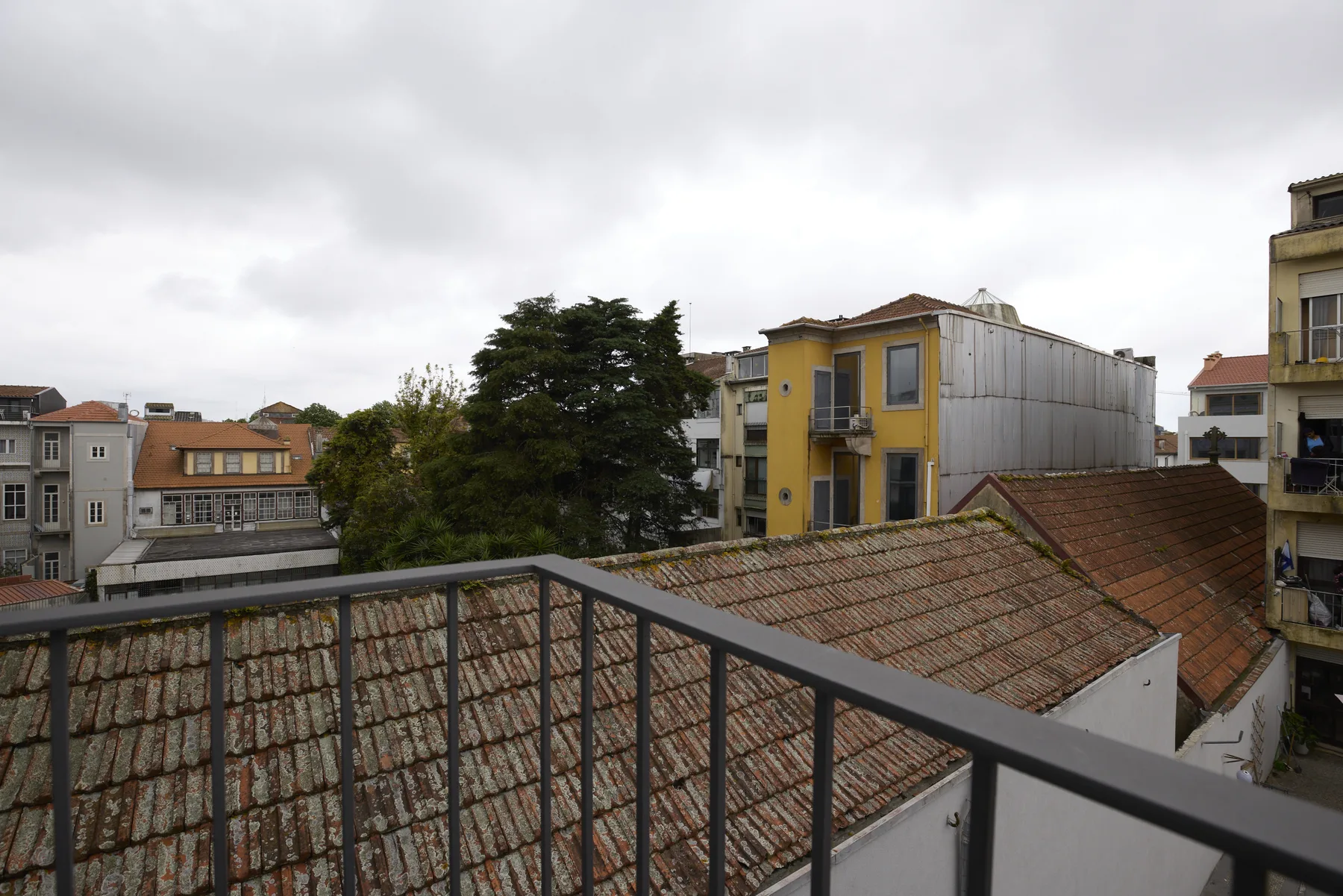 Un balcón da a tejados de tejas y edificios cercanos bajo un cielo nublado.