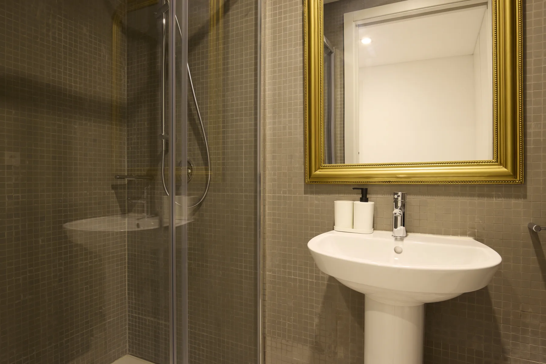 Baño alicatado con lavabo de pedestal, espejo y ducha.