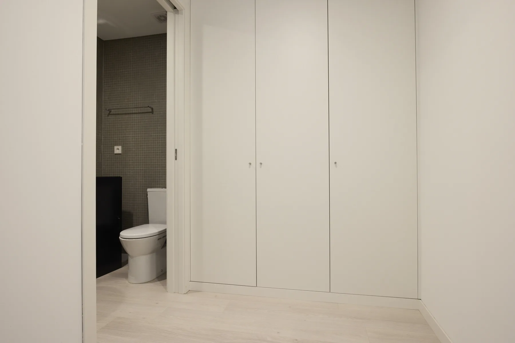 Un baño con un inodoro junto a una pared de armarios blancos.