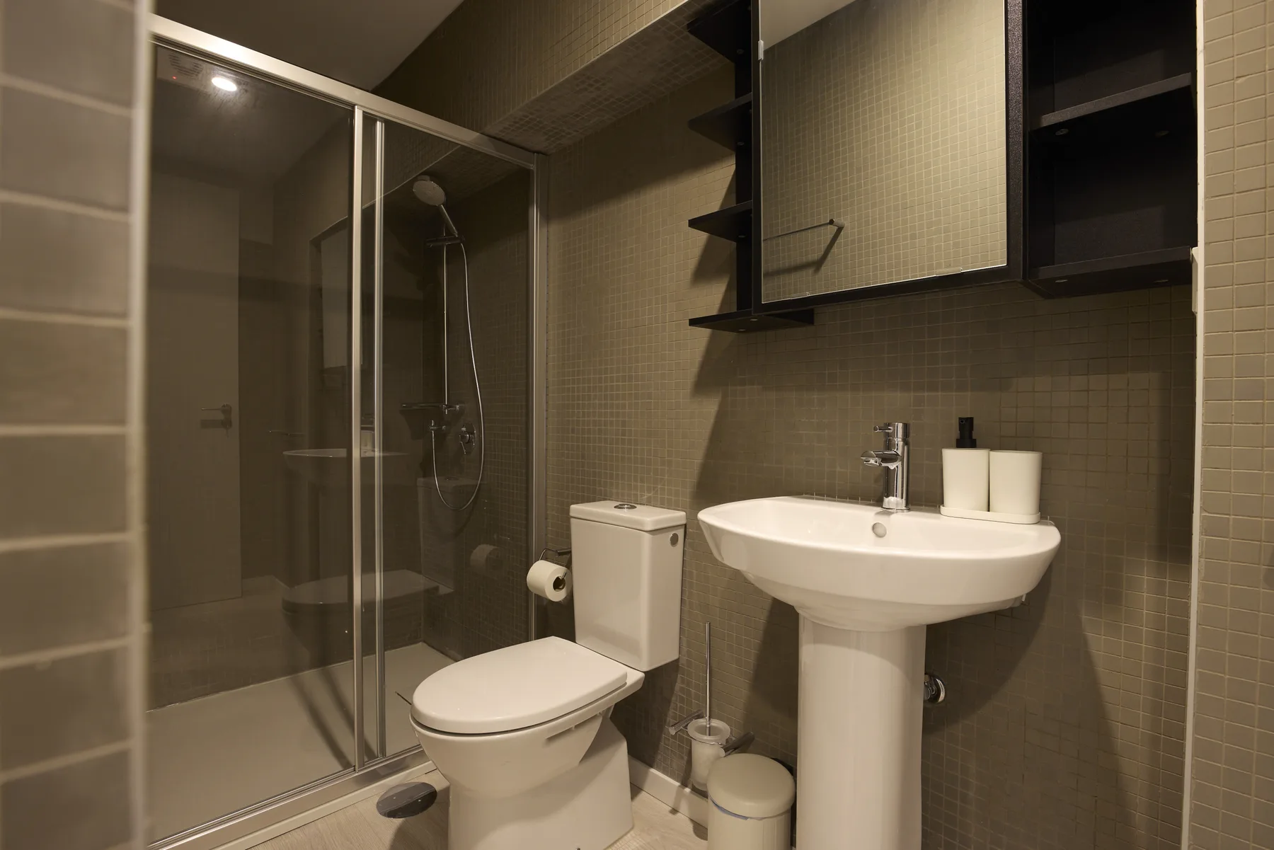 Un baño alicatado con ducha acristalada, inodoro y lavabo con pedestal.