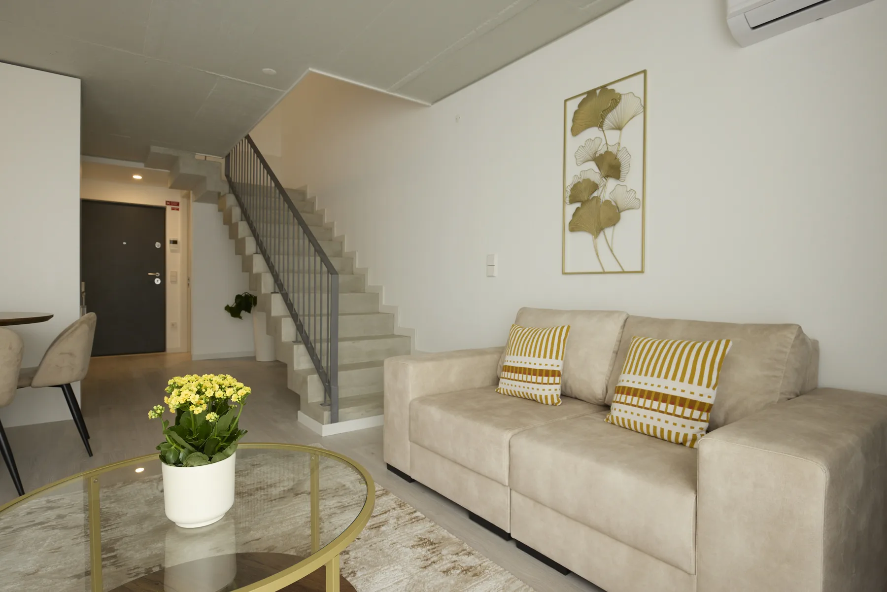 Sala de estar con sofá, mesa de centro de vidrio y escalera.