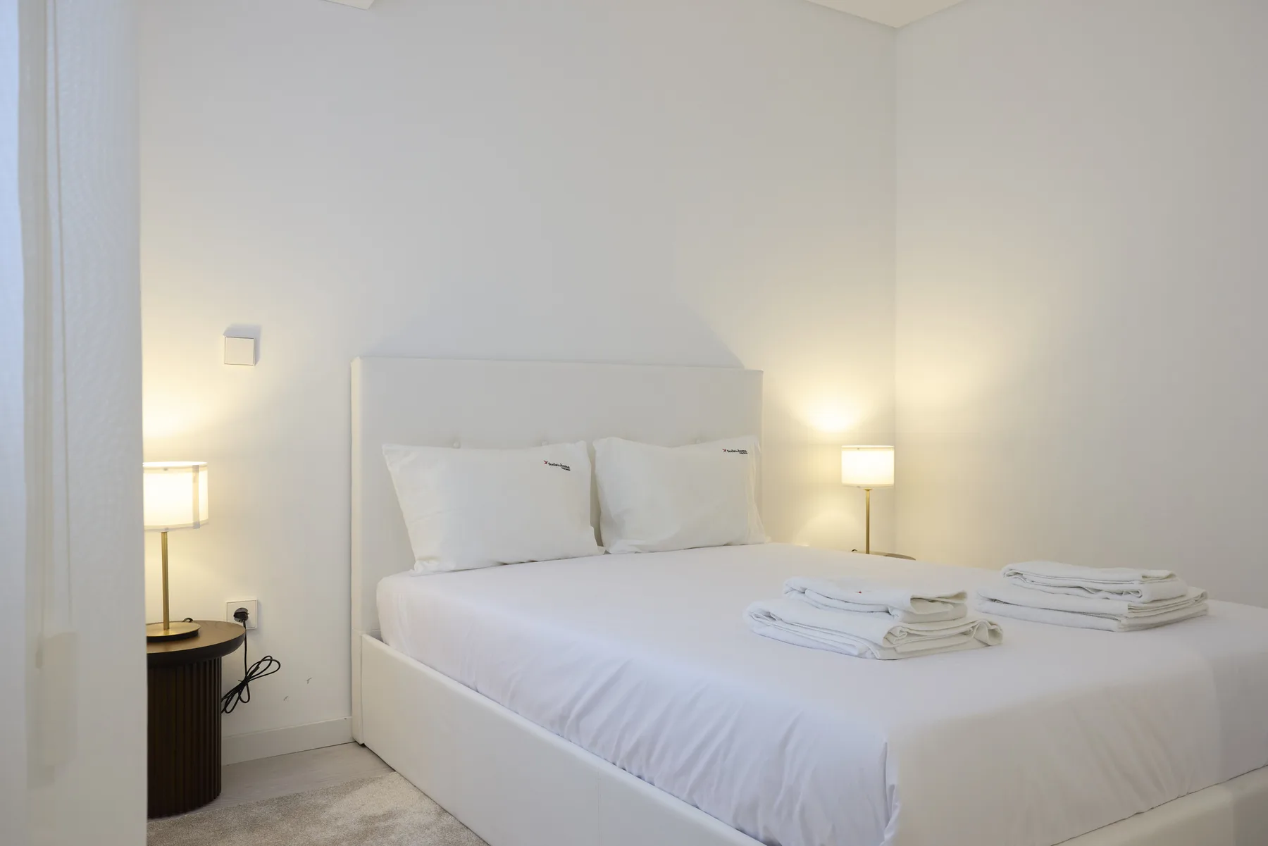 Un dormitorio luminoso con una cama blanca y lámparas a los lados.
