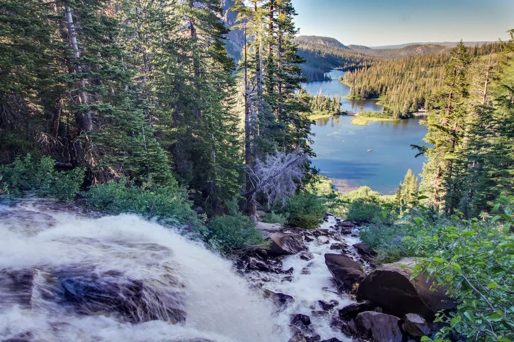 A waterfall rushes through a forest toward a blue lake.