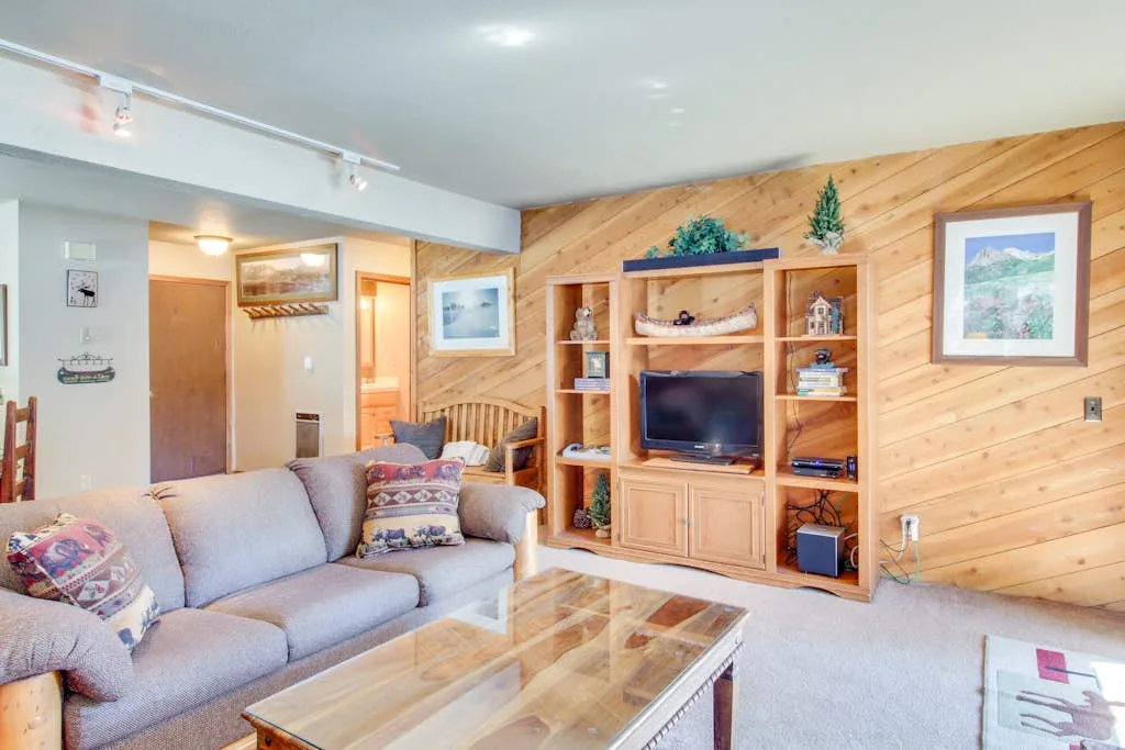A living room with a sectional sofa, glass coffee table, and wooden entertainment center.