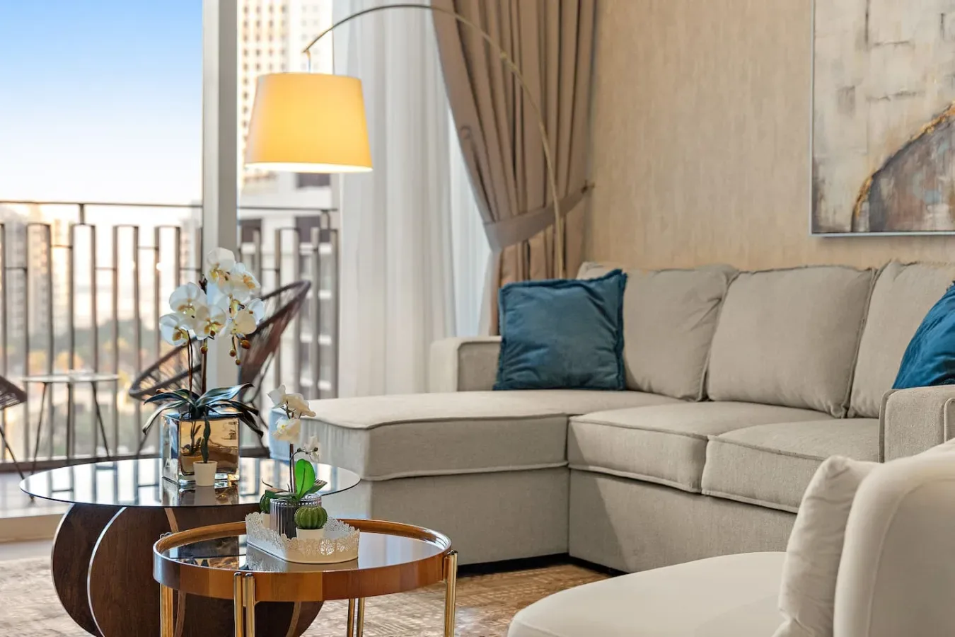 Sala de estar con asientos beige, una mesa de centro de vidrio y vista al balcón.