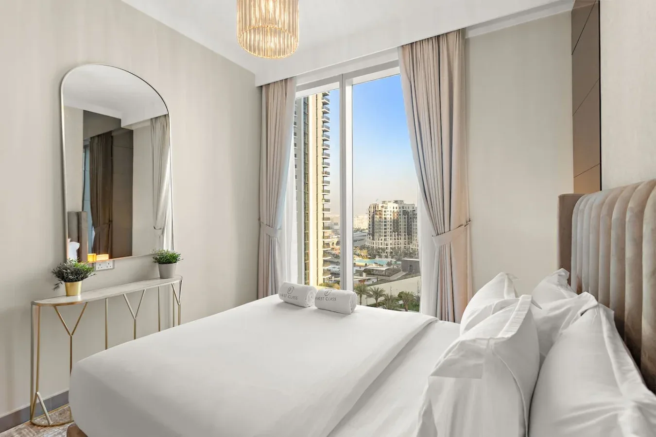 Un dormitorio luminoso con una cama bien hecha junto a una ventana grande con vistas a edificios.