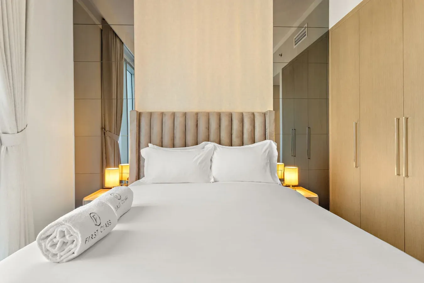 Una cama de dormitorio bien arreglada, con almohadas blancas y una toalla enrollada.