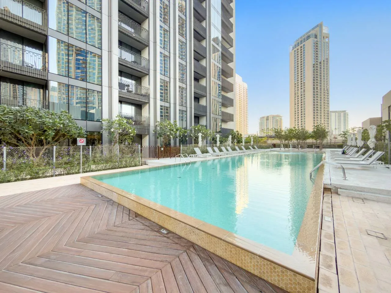 Una piscina al aire libre junto a edificios modernos, con tumbonas alrededor.
