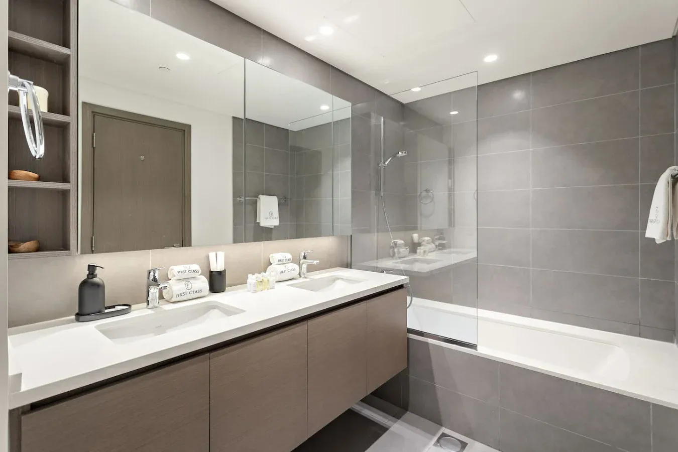 Un baño moderno con un lavabo doble largo y una bañera detrás de una mampara de vidrio.