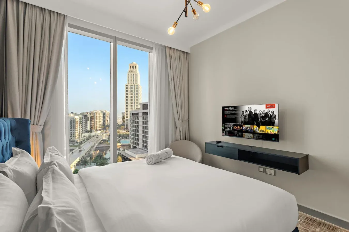 Un dormitorio luminoso con una cama grande junto a ventanales con vistas a la ciudad.