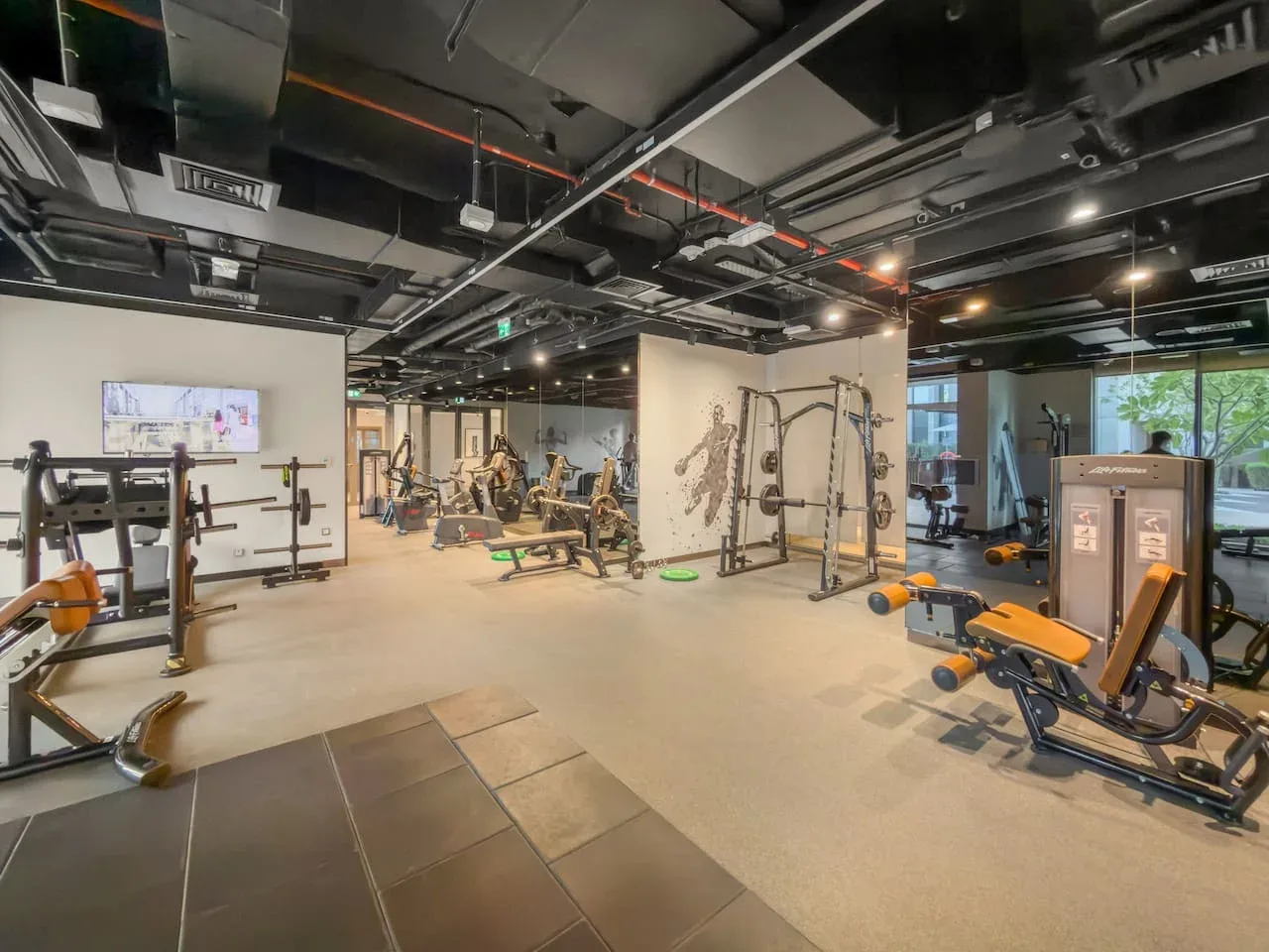 Un gimnasio amplio con máquinas de ejercicio, pesas y una pantalla en la pared.