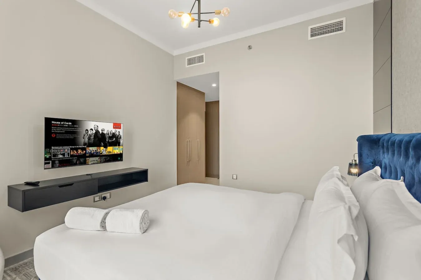 Un dormitorio con una cama tendida, un televisor en la pared y una luz junto a la cama.
