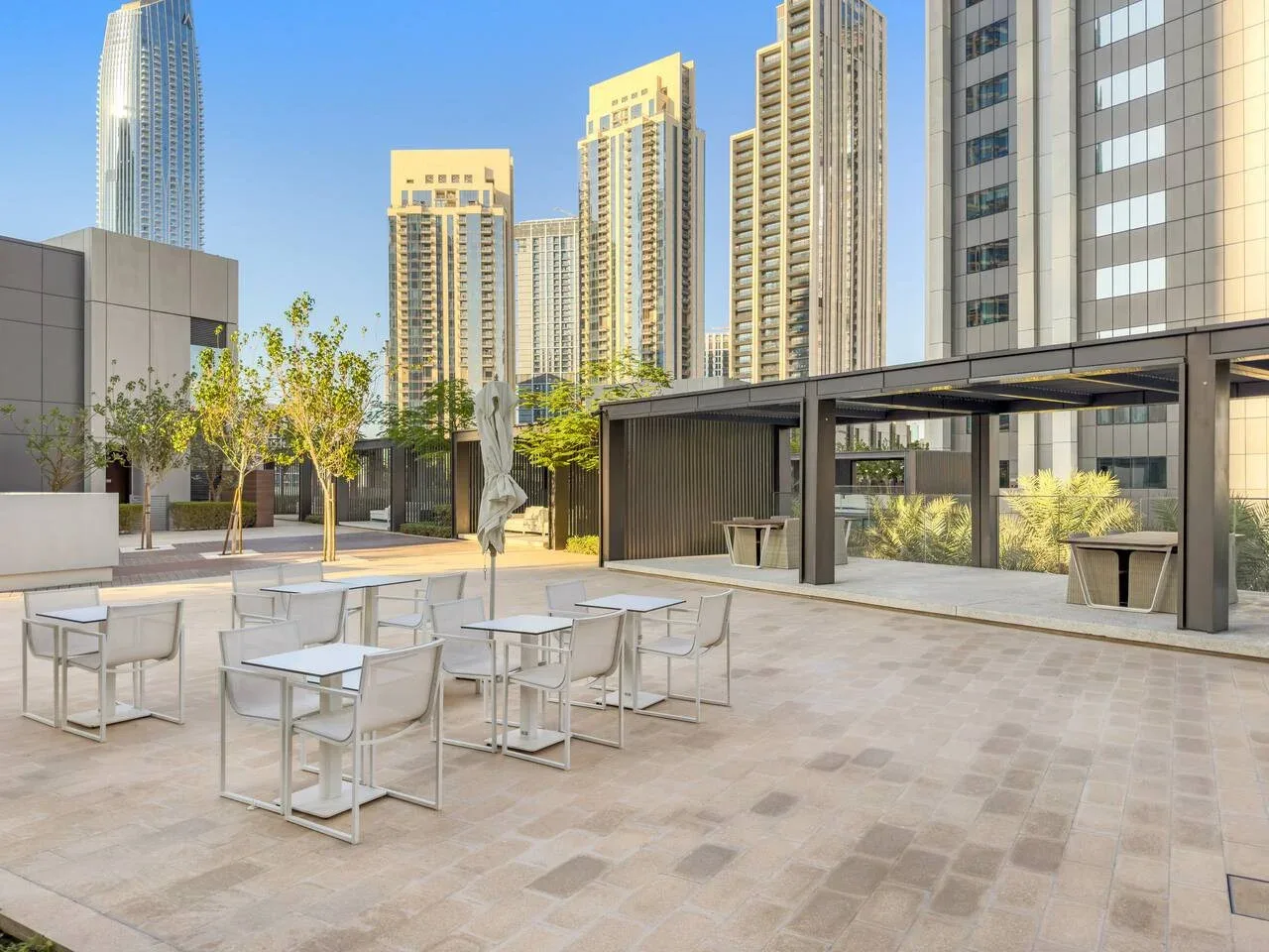 Una terraza al aire libre con mesas y asientos junto a edificios altos modernos.