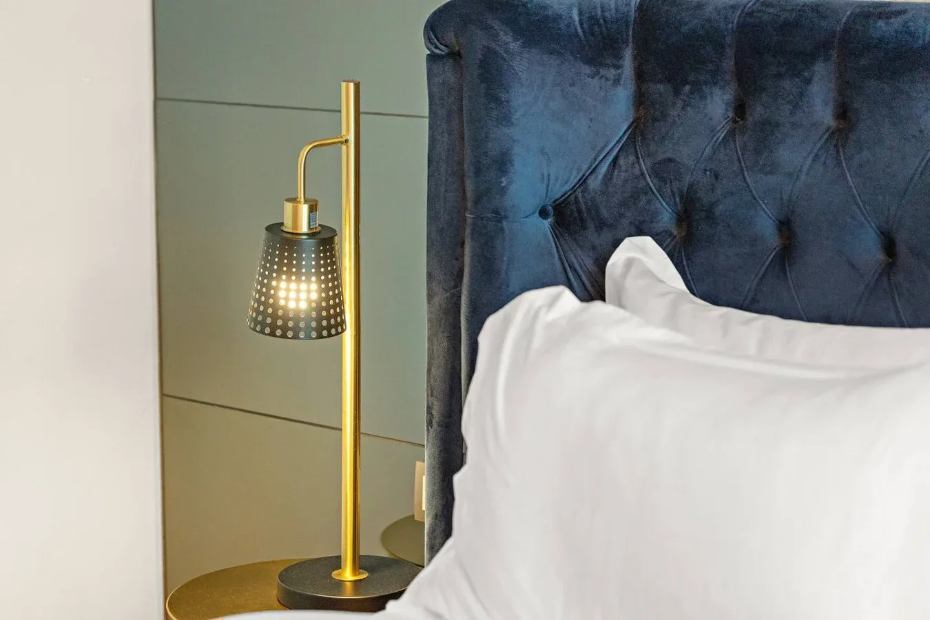 Un dormitorio con almohadas blancas junto a una lámpara dorada de noche.